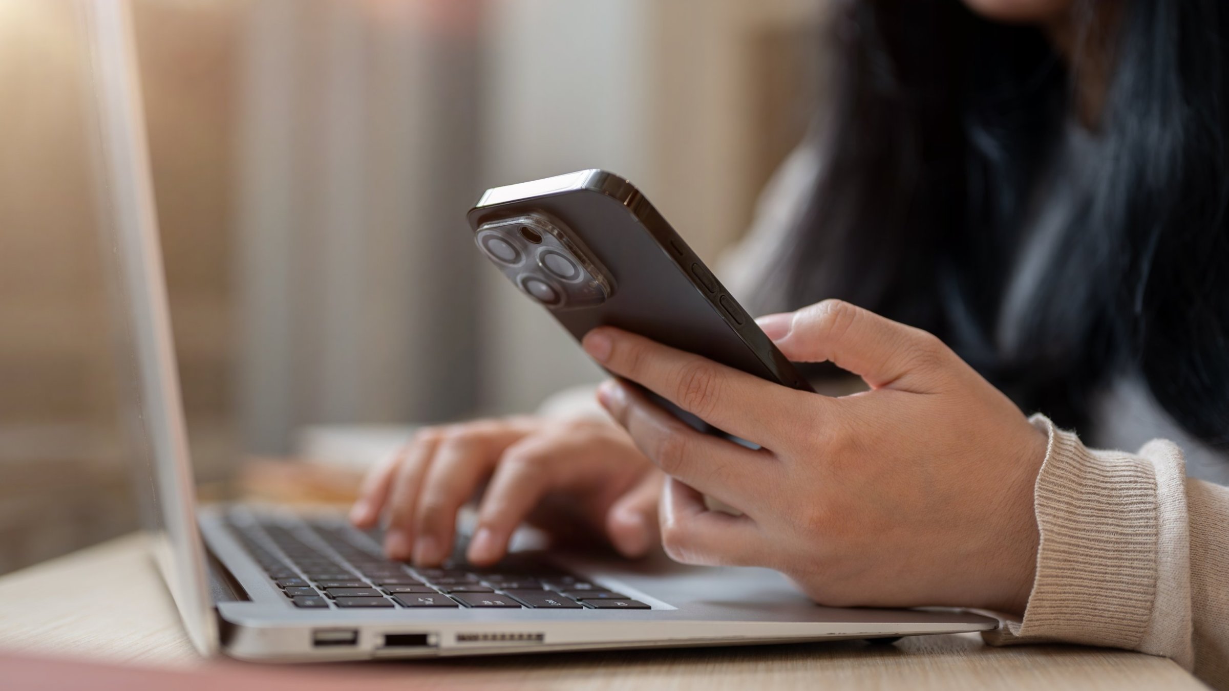 A woman uses her smartphone while working on her laptop. (Shutterstock Photo)